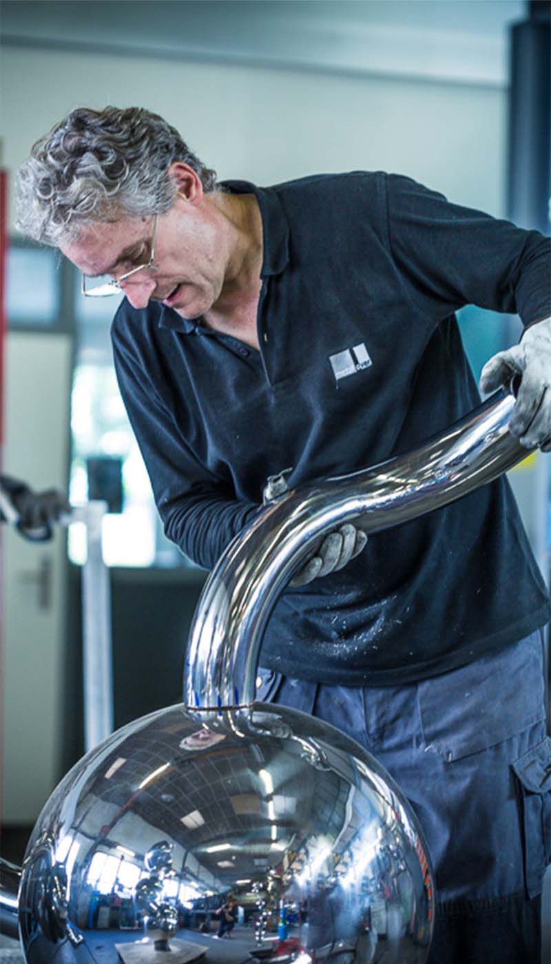 Person in workshop working on curved stainless steel tube attached to polished stainless steel sphere