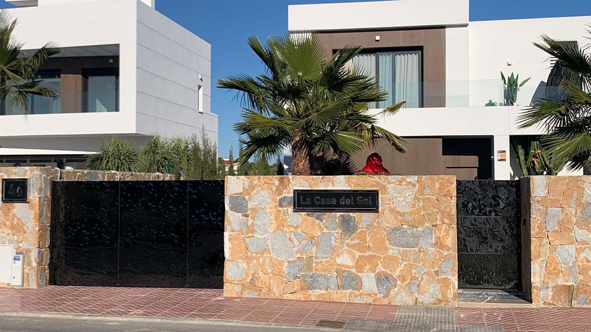 Modern villa with black stainless steel entrance gate and natural stone wall with “La Casa del Sol” sign