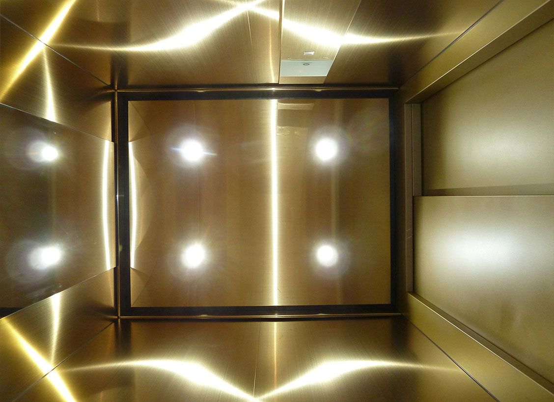 Ceiling view of gold-coloured Oro HL stainless steel lift cabin with integrated spotlights