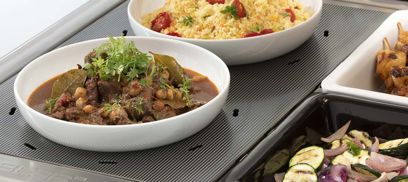 Bowls with hot dishes on ribbed stainless steel warming plate in display