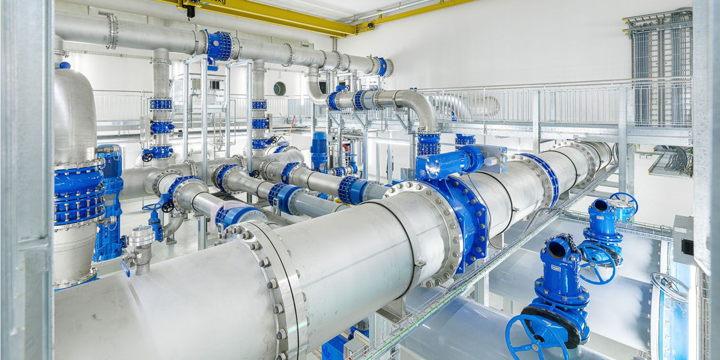 Edelstahl-Rohrleitungen mit blauen Flanschen und Armaturen in einem hellen Technikraum