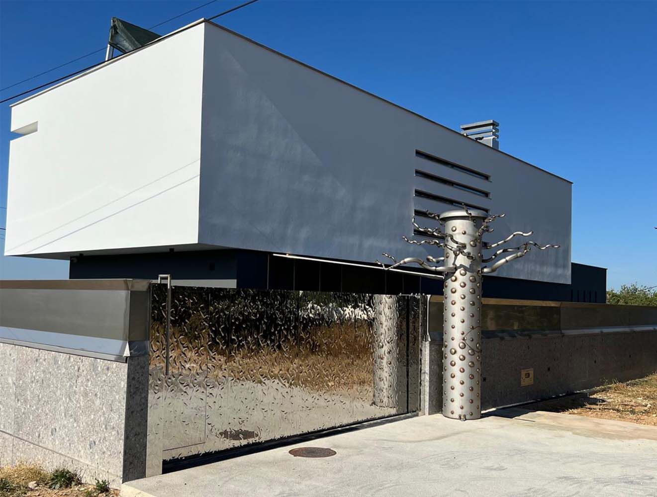 Modernes Einfahrtstor mit spiegelnder, wellenförmig strukturierter Edelstahloberfläche vor weissem Gebäude bei Tageslicht