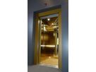 Open lift cabin with gold-coloured Oro HL stainless steel and matching door frame