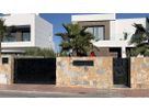 Modern black stainless steel entrance gate between natural stone walls with villa in the background