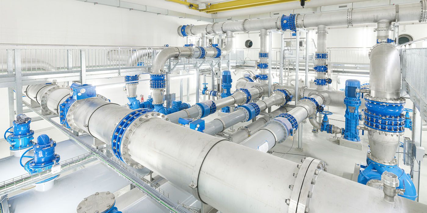 Mehrere Edelstahl-Rohrleitungen mit blauen Flanschen und Armaturen in einer technischen Anlage