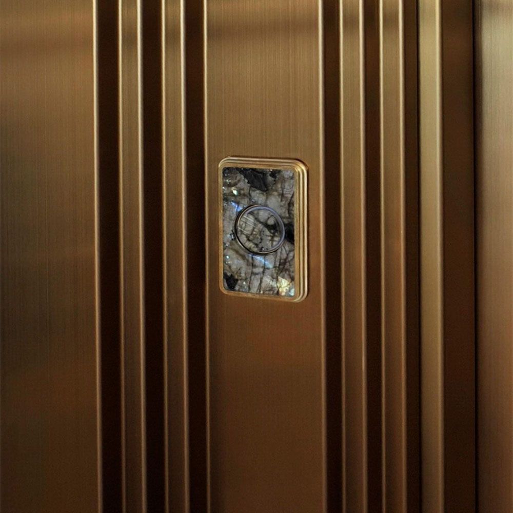Gold-coloured stainless steel lift door with vertical profile structure and integrated viewing window