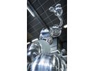 Polished stainless steel spheres and curved tube segment in a workshop hall with ceiling lighting