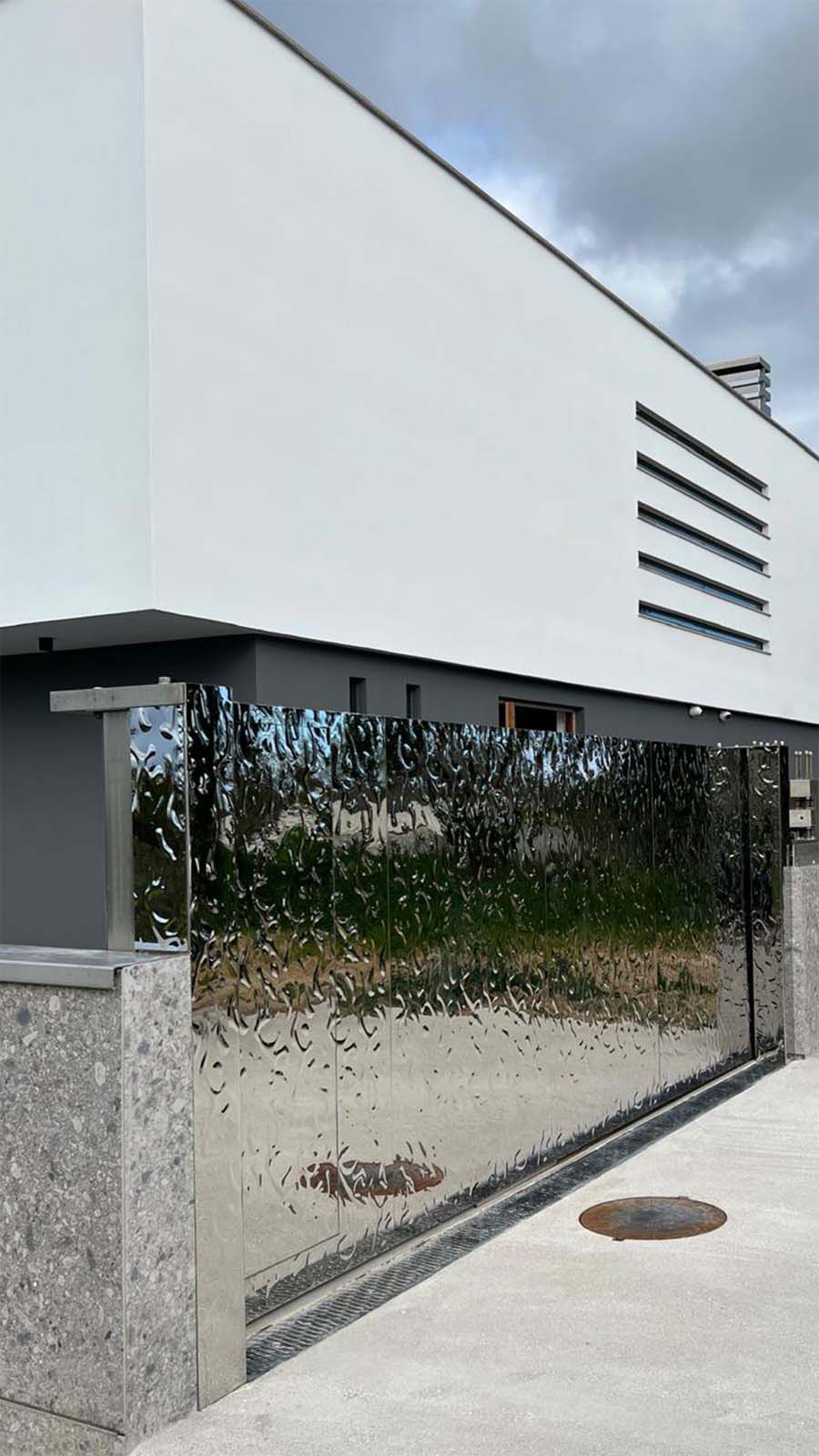 Modernes Einfahrtstor mit spiegelnder Edelstahloberfläche in Wellenstruktur an weissem Gebäude