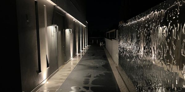 Einfahrtstor mit wellenförmig strukturierter Edelstahloberfläche entlang eines beleuchteten Gehwegs bei Nacht