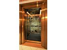 Lift installation with gold-coloured stainless steel doors and three-dimensional frames in front of natural stone wall